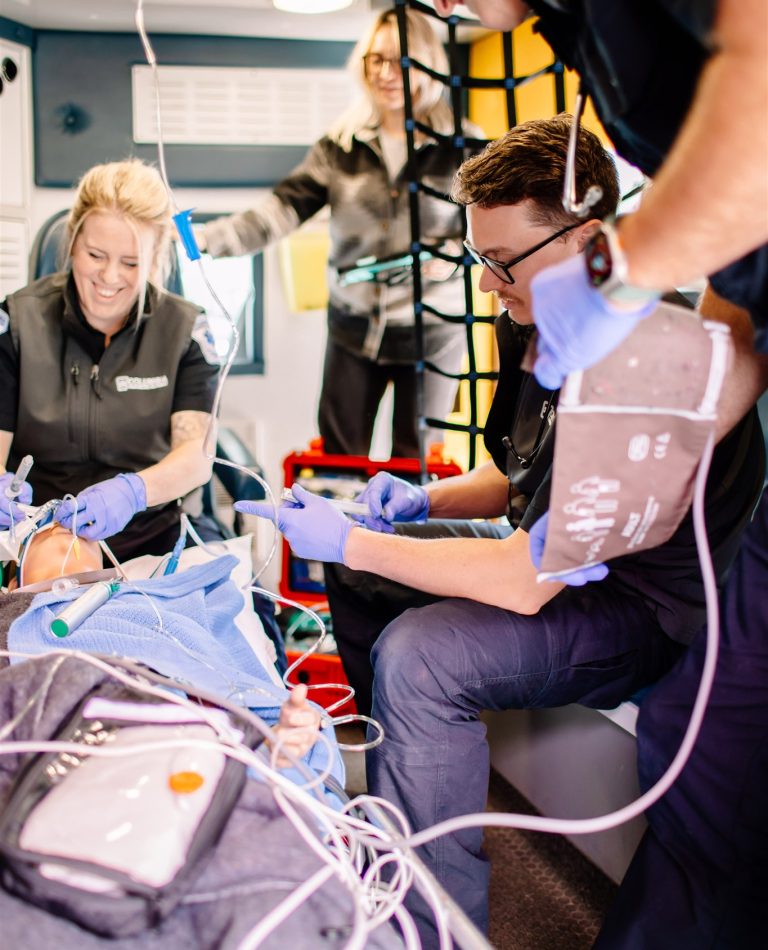 Paramedic students practice their skills on a mannikin on a stretcher in an ambulance