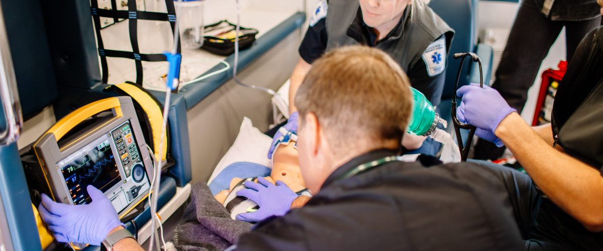 Paramedic students inside an ambulance using simulated medical equipment.