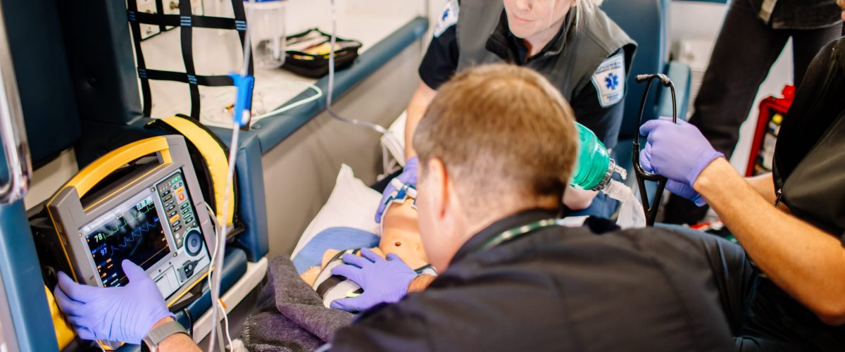 Paramedic students inside an ambulance using simulated medical equipment.